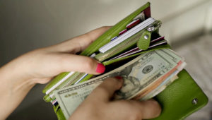 Girl with pink nail opening her green purse with credit cards and money from different countries