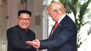 Líder de Corea del Norte, Kim Jong Un, con una amplia sonrisa, estrecha la mano del presidente de Estados Unidos, Donald Trump, quien lo mira e invita a caminar.