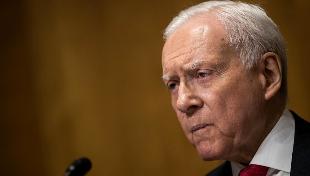 Senador republicano Orrin Hatch, frente a un micrófono mirando al público con seriedad.