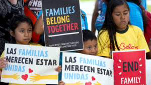 Niños migrantes mostrando carteles en inglés y español en los que piden que las familias tienen que estar unidas.