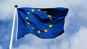 Bandera de la Unión Europea flameando delante de un cielo azul con nubes.