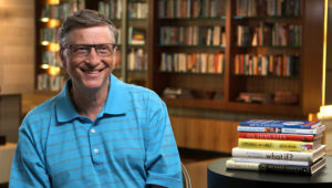Bill Gates sonriendo en su biblioteca personal, junto con un grupo de libros en su mesa. Foto: The Gates Notes.