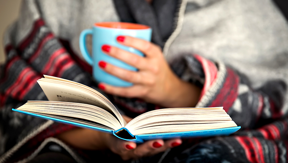 woman reading a book and holding a mug of hot beverage; Shutterstock ID 326453363; PO: today.com
