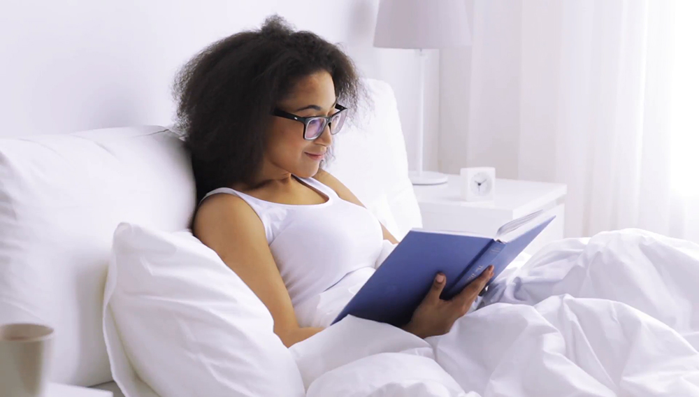 Rest, comfort and people concept - young african woman reading book in bed at home
