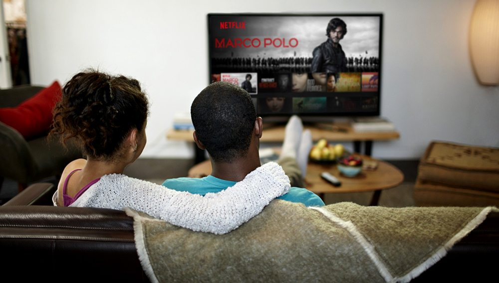 Un hombre y una mujer en una sala de estar viendo Netflix en un televisor grande. Image Credit: Netflix.com