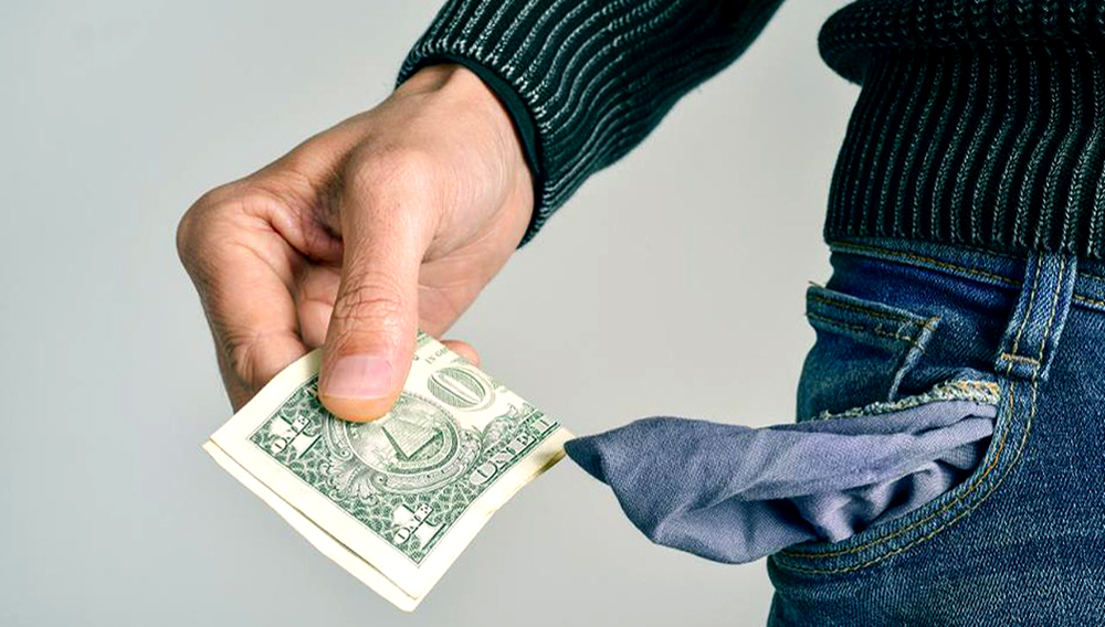 Foto de archivo - Un hombre caucásico joven en pantalones vaqueros toma un dólar de su bolsillo. 123rf.com