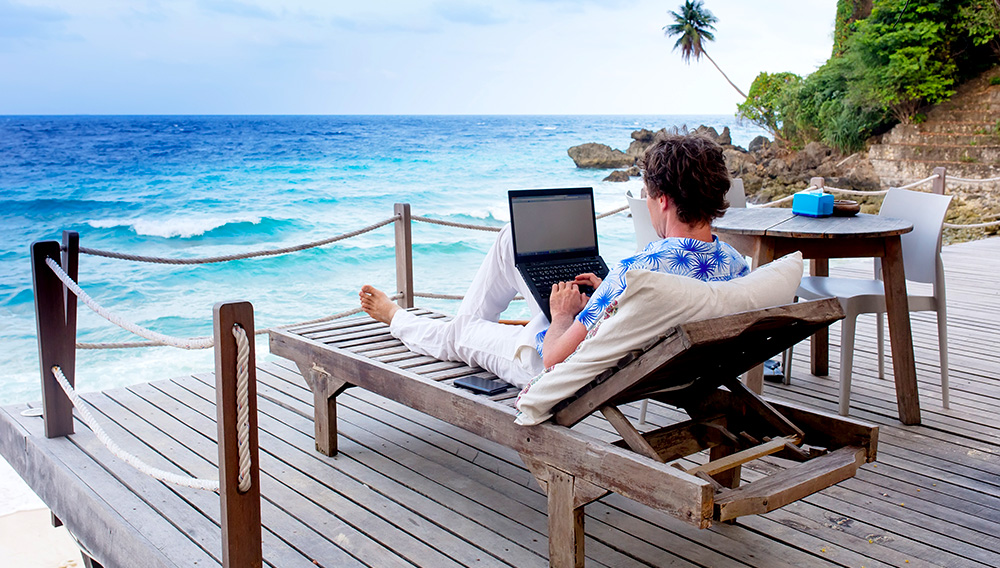 Joven usando una laptop en un lugar con vista al mar. Foto: Shutterstock
