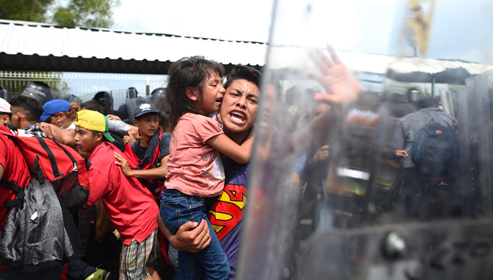 Un migrante hondureño con una menor en brazos grita hacia los miembros de la policía mexicana en el paso fronterizo entre Guatemala y México en Tecún Umán, Guatemala. EFE