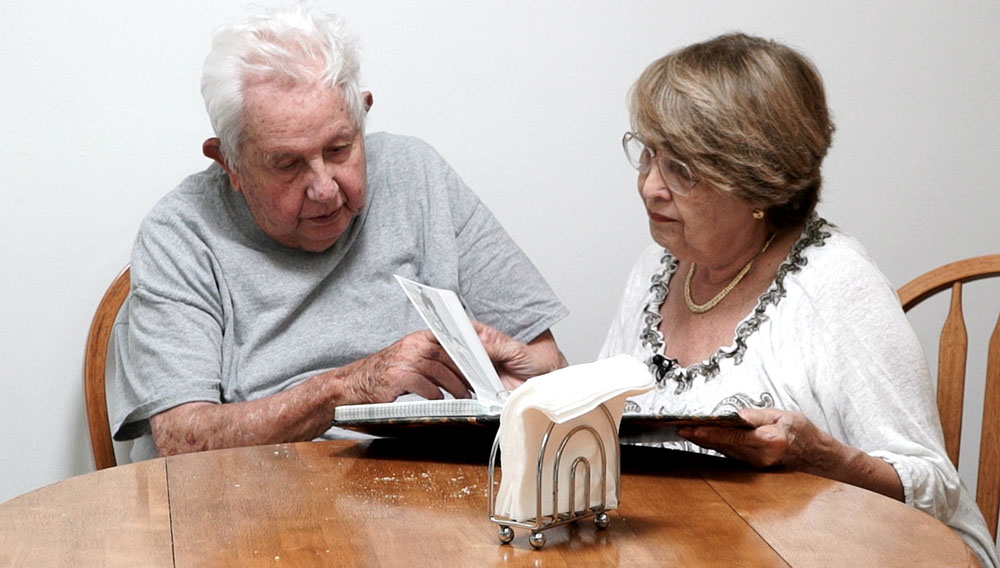 Un anciano que está al cuidado de una mujer también adulta que está revisando un libro.