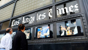In this May 16, 2016, file photo, pedestrians look at news photos posted outside the Los Angeles Times building in downtown Los Angeles. The Los Angeles Times suspended the head of its Beijing bureau Wednesday, May 16, 2018, after he was accused of sexual misconduct for a second time. (AP Photo/Richard Vogel, File)