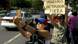 Una miembro de la oposición se toma una selfie junto a una mujer sosteniendo un cartel durante una protesta en Caracas, Venezuela, el viernes 11 de enero de 2019. (AP Foto/Fernando Llano)