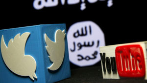 A 3D plastic representation of the Twitter and Youtube logo is seen in front of a Daesh flag. Photo: Sputnik International