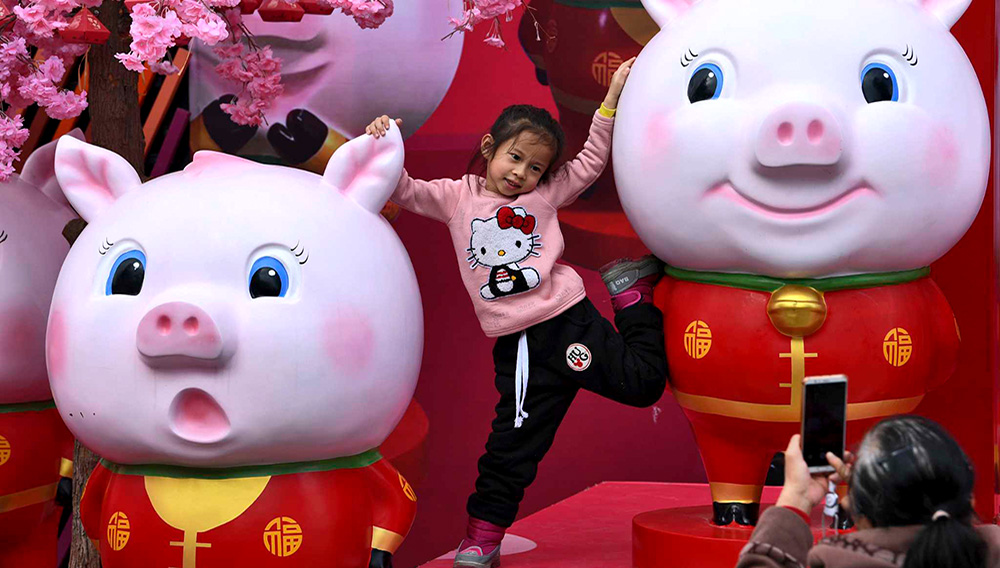 Fotografía del 28 de enero de 2019 de una niña china posando para una foto entre esculturas de cerdos exhibidas afuera de un centro comercial en Nanning, en la región autónoma Guangxi Zhuang en el sur de China. (Chinatopix vía AP)