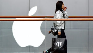 Una mujer con una bolsa de la cadena de tiendas de moda estadounidense Abercrombie & Fitch pasa por delante de una tienda de Apple en un centro comercial de Beijing, en China, el 26 de febrero de 2019. (AP Foto/Andy Wong)