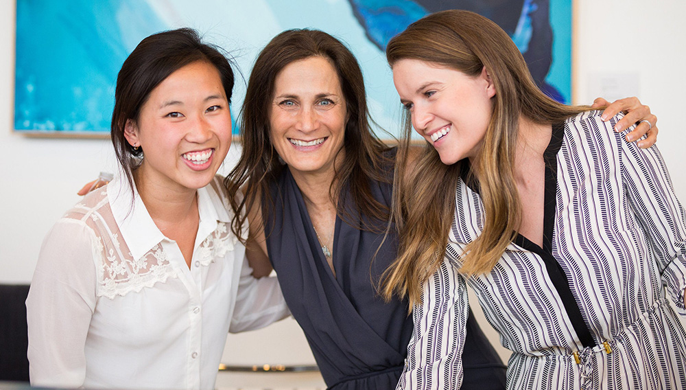 Tres mujeres de distintas edades y razas sonriendo juntas en una oficina | modernwell.co