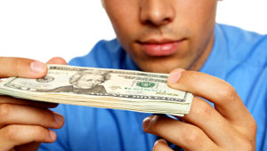Hombre joven pensativo en camisa azul mirando billetes. | Foto Stock