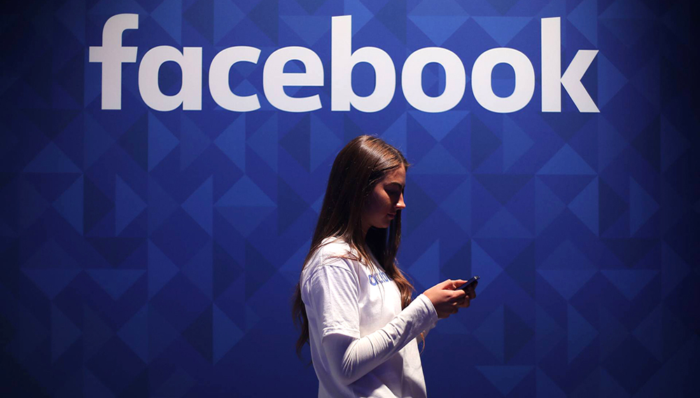 File photo dated 03/11/15 of a woman using her phone under a Facebook logo, as the social media giant has backed the Government's new online safety lessons to help school pupils recognise online dangers.