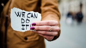 Closeup de uma jovem mulher caucasiana na rua mostrando um pedaço de papel com o texto "We can do it". | Photostock