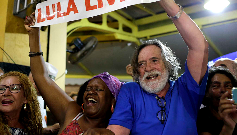 El actor brasileño Jose de Abreu, derecha, y una mujer sostienen un cartel con la leyenda "Lula Libre" al arribar al bar Amarelinho en Río de Janeiro, Brasil, 8 de marzo de 2019. (AP Foto/Silvia Izquierdo)