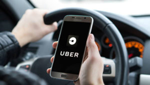 Conductor de un automóvil con un smartphone en la mano derecha que tiene el logotipo de Uber en su pantalla. Foto: Uber