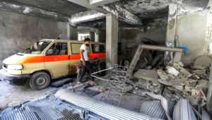 A man walks past a damaged mini-van that was used as a make-shift ambulance amidst debris in the garage of a hospital damaged after a reported air strike in Jisr Al Shughur in the northeastern Syrian Idlib province on July 10, 2019. | AFP