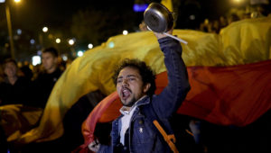 An anti-government protester waves a pot in Bogota, Colombia, Saturday, Nov. 23, 2019. Authorities in Colombia are maintaining a heightened police and military presence in the nation's capital following two days of unrest. (AP Photo/Ivan Valencia)