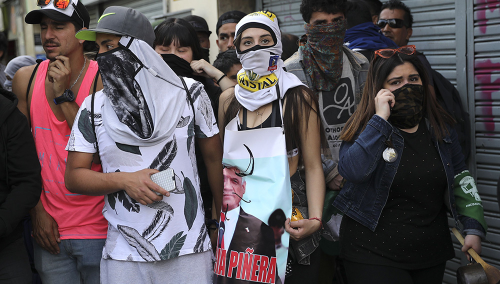 A demonstrator holds a defaced poster of Chile's President Sebastian Pinera during protests in Santiago, Chile, Wednesday, Oct. 23, 2019. Rioting, arson attacks and violent clashes wracked Chile as the government raised the death toll in an upheaval that has almost paralyzed the South American country long seen as the region's oasis of stability. (AP Photo/Rodrigo Abd)