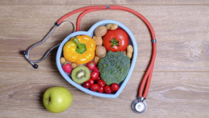 Heart shaped dish with vegetables and stethoscope isolated on wooden background. Photo: Adobe stock