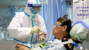 A nurse in a protective suit feeds a coronavirus patient inside an isolated ward at Zhongnan Hospital of Wuhan University on February 8, 2020. | China Daily via Reuters