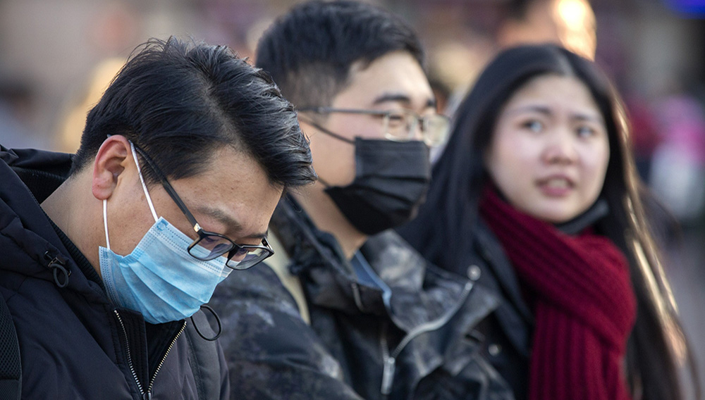 Travelers wear face masks as they walk outside of the Beijing Railway Station in Beijing, Monday, Jan. 20, 2020. (AP Photo/Mark Schiefelbein)