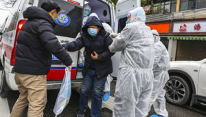 This photo taken on January 26, 2020 shows a patient assisted by medical staff members wearing protective clothing to help stop the spread of a deadly virus which began in the city, as he gets off an ambulance in Wuhan in China's central Hubei province. (Photo by STR/AFP) / China OUT
