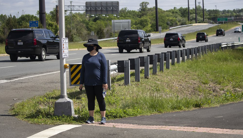 A woman wears a mask as she waits for the motorcade for President Donald Trump to go past, Saturday, May 23, 2020, in Sterling, Va. Trump is en route to Trump National Golf Club. (AP Photo/Alex Brandon)