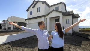 In this April 27, 2019, photo, Andy and Stacie Proctor stand in front of their new home in Vineyard, Utah. For some millennials looking to buy their first home, the hunt feels like a race against the clock. The Proctors ultimately made a successful offer on a three-bedroom house for $438,000 in Vineyard. (AP Photo/Rick Bowmer)