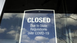 In this Wednesday, April 22, 2020 photo a closed sign is posted in the window of a store because of the coronavirus, in an outdoor mall, in Dedham, Mass. (AP Photo/Steven Senne)