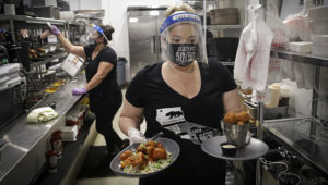 A waitress takes a food order from the kitchen at Slater's 50/50 Wednesday, July 1, 2020, in Santa Clarita, California. (AP Photo/Marcio Jose Sanchez)