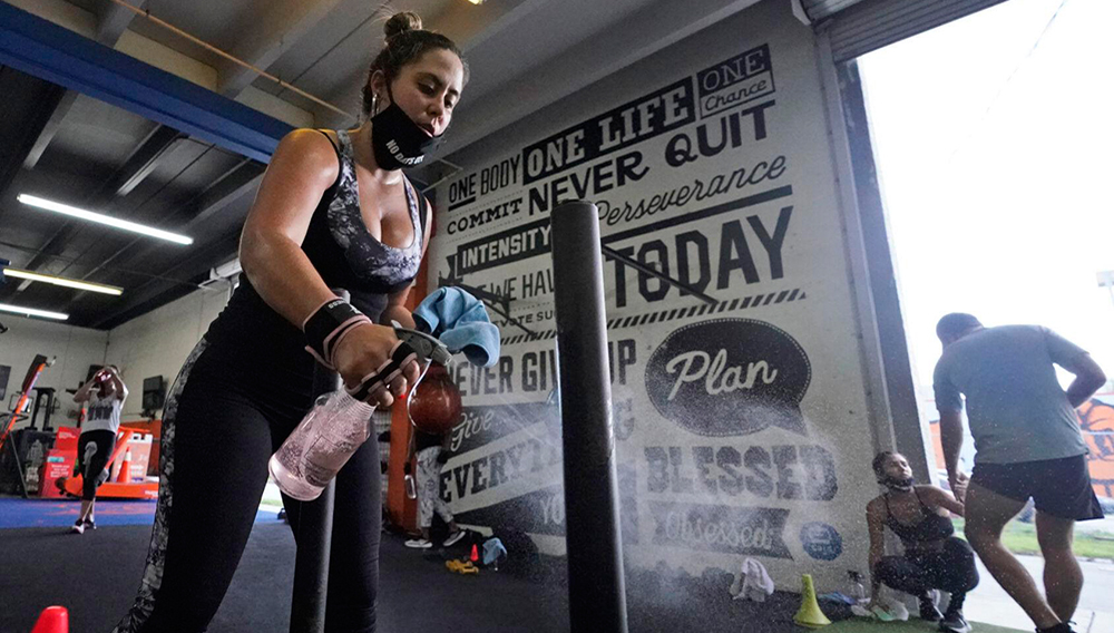 Giannina Nicoletti sanitizes a piece of equipment as she works out, Monday, Aug. 31, 2020, at Legacy Fit in the Wynwood Art District of Miami. As the vast majority of in-person fitness clubs switched to virtual classes when the pandemic hit, Legacy Fit took the opposite approach. (AP Photo/Wilfredo Lee)