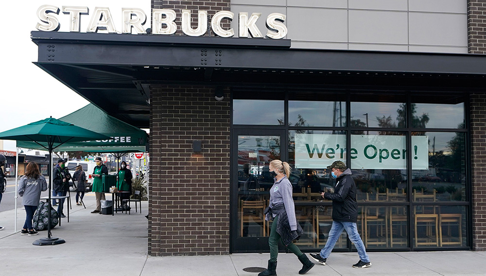Customers walk past a sign that reads "We're Open!" at a Starbucks Coffee store in south Seattle, Tuesday, Oct. 27, 2020. Starbucks saw faster-than-expected recovery in the U.S. and China in its fiscal fourth quarter, giving it confidence as it heads into the holiday season. (AP Photo/Ted S. Warren)