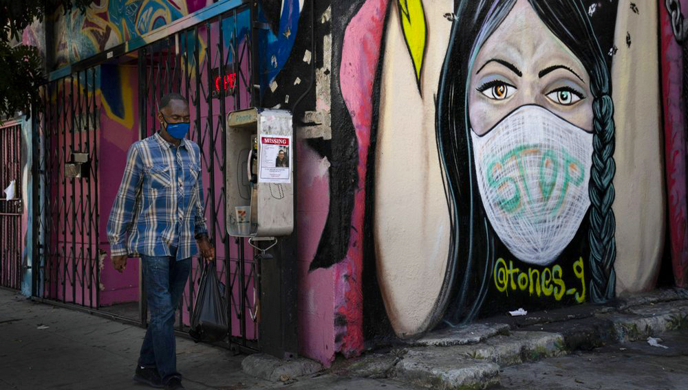 FILE - In this Oct. 1, 2020, file photo, a man wearing a face mask walks past a mural in South Central Los Angeles. President Donald Trump’s startling COVID-19 diagnosis serves as a cruel reminder of the pervasive spread of the coronavirus in the United States and shows how tenuous of a grip the nation has on the crisis, health experts said. (AP Photo/Jae C. Hong, File)