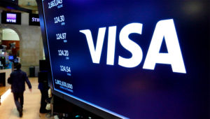 FILE- In this April 23, 2018, file photo, the logo for Visa appears above a trading post on the floor of the New York Stock Exchange. Visa Inc. said Wednesday, Oct. 28, 2020, that its fiscal fourth quarter profits dropped 29% due to fewer dollars crossing on its namesake payment network while the world was in the grips of a pandemic-caused recession. (AP Photo/Richard Drew, File)