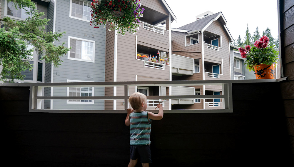 Grigory Vodolazov's 3-year-old son peers into his family's apartment complex from their unit in Bellevue, Washington. | Photo: Jovelle Tamayo for NPR
