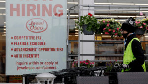 A man pushes carts as a hiring sign shows at a Jewel Osco grocery store in Deerfield, Ill., Thursday, April 23, 2020. Friday, Dec. 4, monthly U.S. jobs report will help answer a key question hanging over the economy: Just how much damage is being caused by the resurgent coronavirus, the resulting restrictions on businesses and the reluctance of consumers to shop, travel and dine out? (AP Photo/Nam Y. Huh)