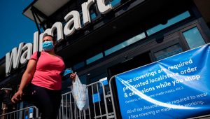 A woman wearing a face mask walks past a sign informing customers that face coverings are required in front of a Walmart store in Washington, DC on July 15, 2020. | Andrew Caballero-Reynolds | AFP | Getty Images