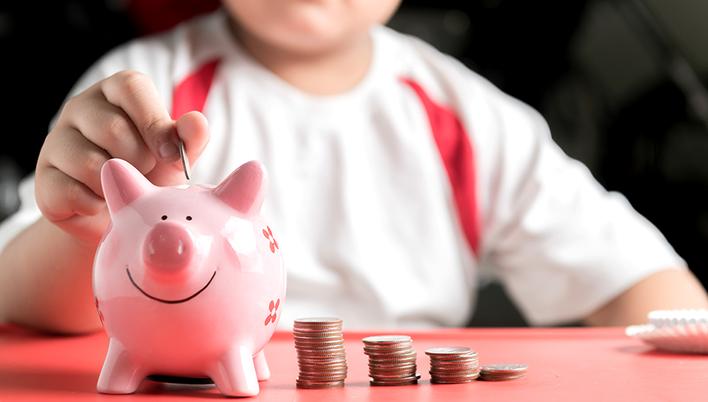 Photo: Hand boy put coin to piggy bank, saving money. | Shutterstock