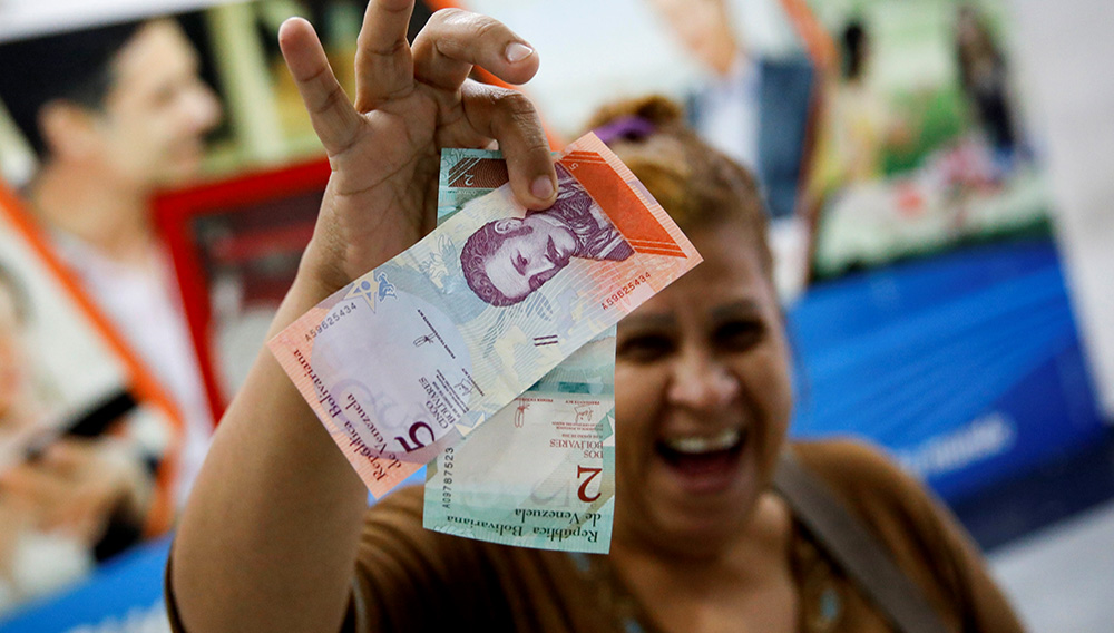 A woman smiles while she shows the new two and five Bolivar Soberano (Sovereign Bolivar) bills, after she withdrew them from an automated teller machine (ATM) at a Mercantil bank branch in Caracas, Venezuela August 20, 2018. REUTERS/Carlos Garcia Rawlins