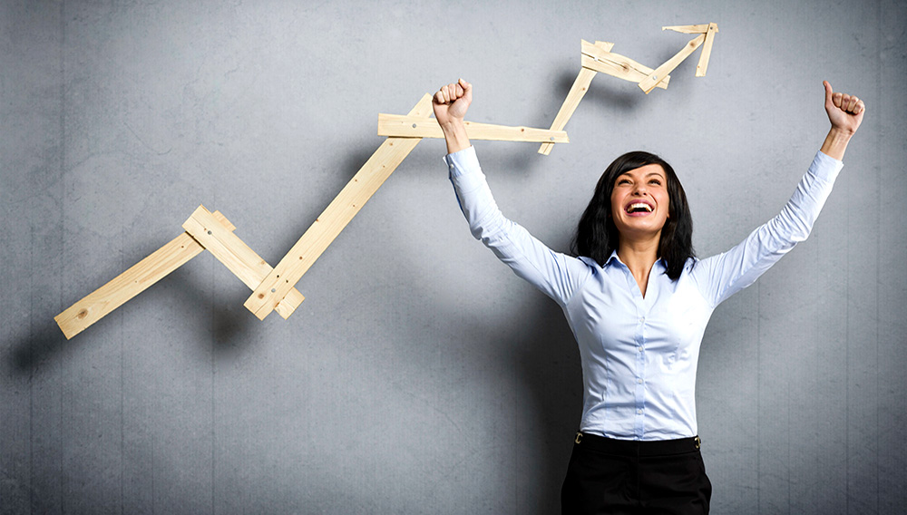 Enthusiastic businesswoman with raised arms cheering in front of positive business graph, isolated on grey background. | BigStock
