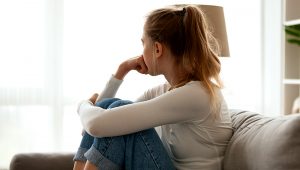 Side view young woman looking away at window sitting on couch at home. | Photo: Shutterstock