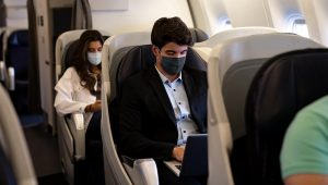 Business man traveling and wearing a facemask on the plane while using his laptop. | iStock