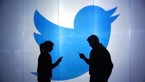 People are seen as silhouettes as they check mobile devices whilst standing against an illuminated wall bearing Twitter Inc.'s logo in this arranged photograph in London, U.K., on Tuesday, Jan. 5, 2016. Photographer: Chris Ratcliffe/Bloomberg via Getty Images
