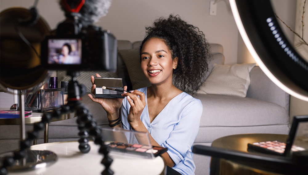 Smiling woman holding a makeup palette while recording her video for blog. Photo: Artem Varnitsin/Adobe Stock.