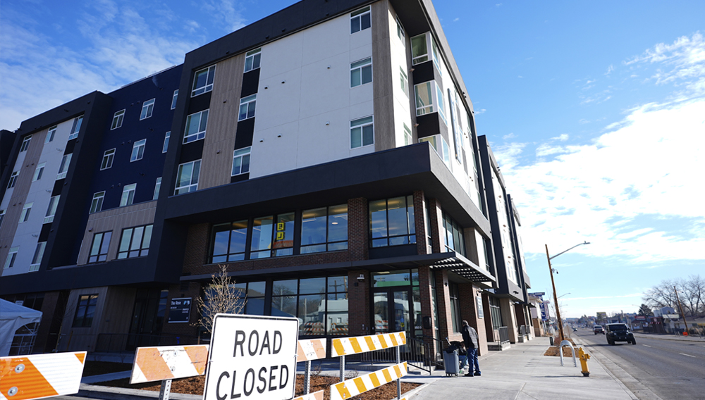 A person sweeps outside during the grand opening of the Rose on Colfax, a new affordable housing community with a co-located childcare center in the East Colfax neighborhood, Jan. 24, 2024, in Denver. (AP Photo/David Zalubowski)